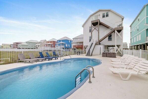 A swimming pool with lounge chairs, a staircase, and a white building with a blue roof.