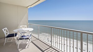 En balkon med et hvidt bord og stole, der ud til en strand med gelænder.