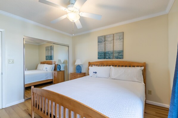 A bedroom with a wooden bed, a ceiling fan, a nightstand with a lamp, and a painting on the wall.