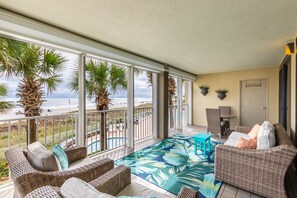 A balcony with wicker furniture, a pool, and a view of the beach.
