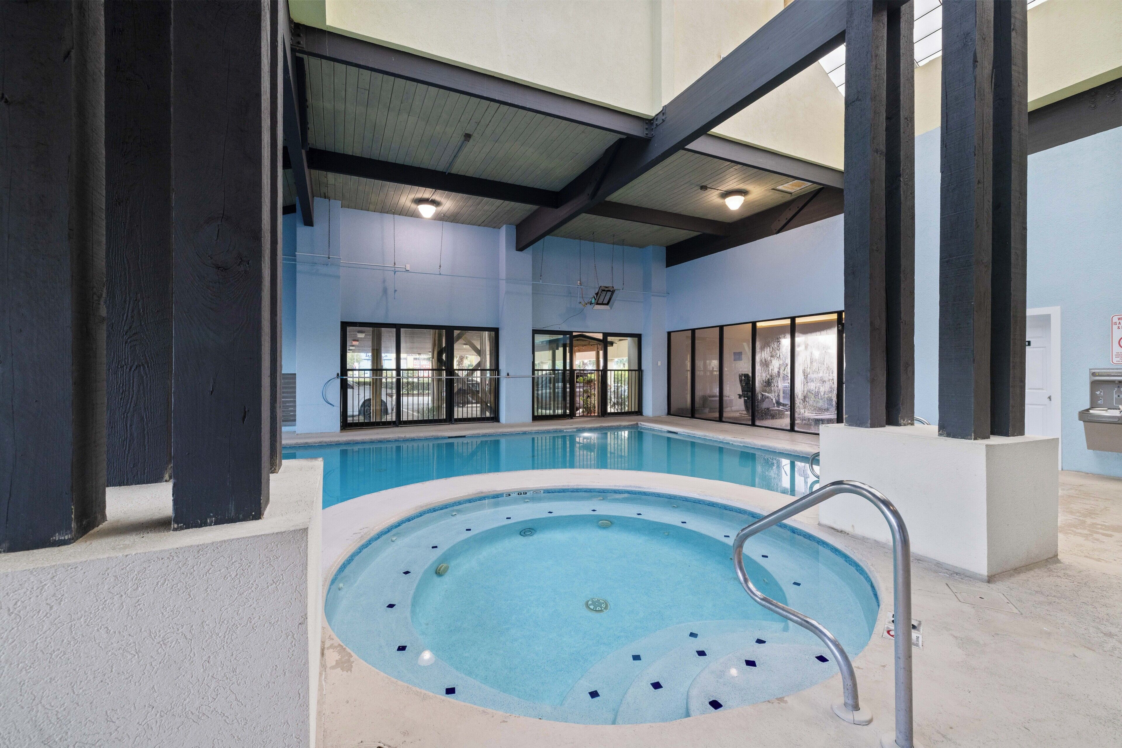 Una piscina interior con jacuzzi, ventanas amplias y un techo con vigas a la vista.