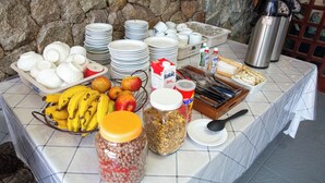 A buffet table with various food items, plates, and utensils. - Pousada Jurerê (Florianópolis)