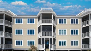 A multi-story residential building with balconies, large windows, and a central entrance.