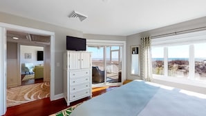 A bedroom with a large bed, a TV on a cabinet, a balcony with a view of the beach, and a door leading to another room. - Captivating oceanfront in this 1st floor condo in Wild Dunes (Island Of Palms)
