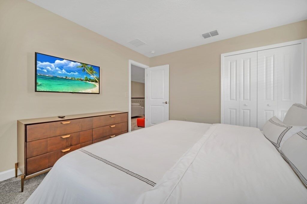 A bedroom with a bed, dresser, and a door leading to another room.
