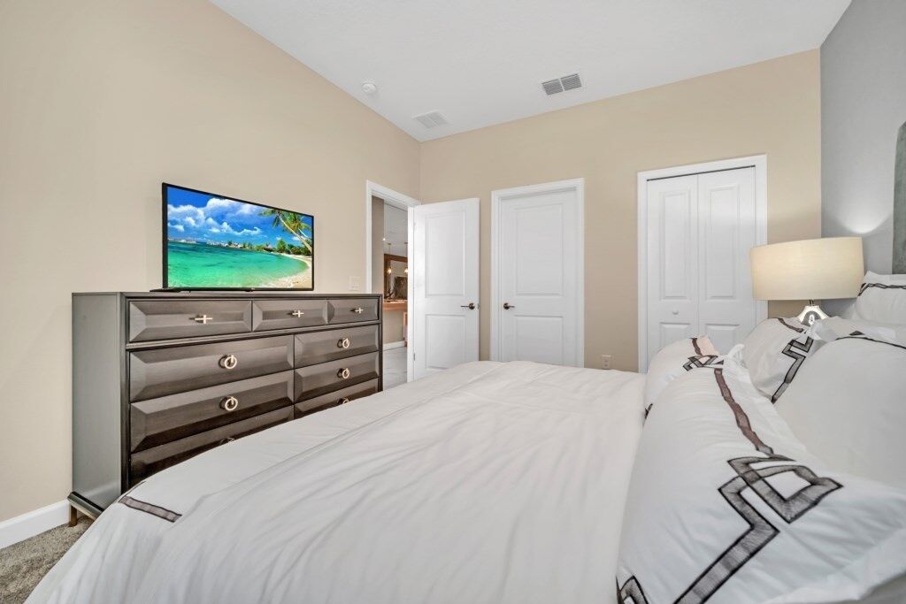 A bedroom with a bed, a dresser, a television, and two doors.