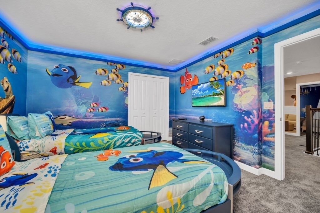 Camera da letto a tema nautico, con un letto decorato con un disegno di pesce, una cassettiera e una porta con un murale a tema marino.
