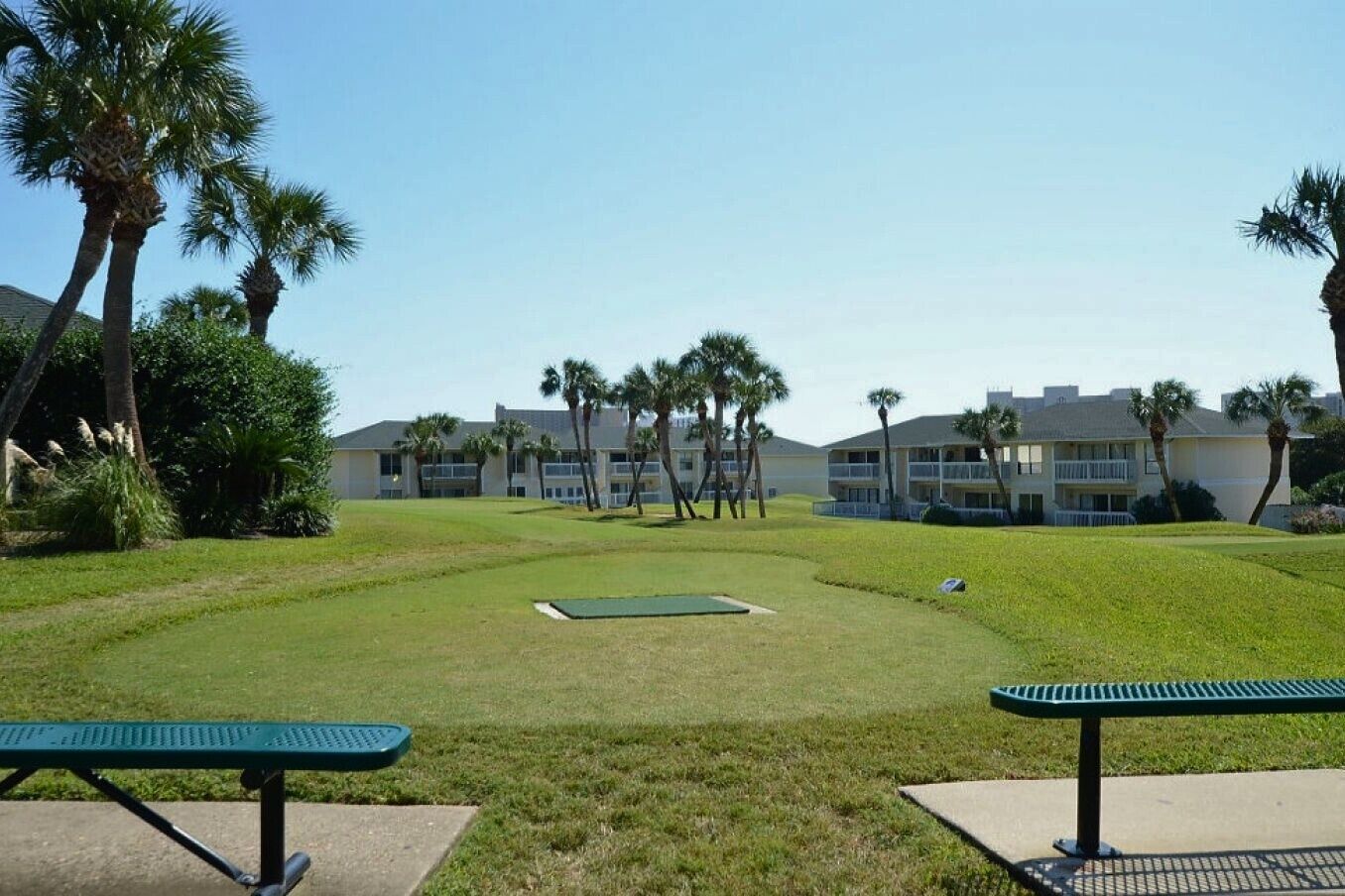 A golf course with a putting green, palm trees, and a building in the background.