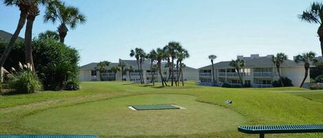 A golf course with a putting green, palm trees, and a building in the background.