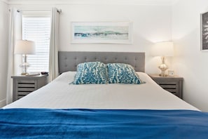 A neatly made bed with a blue and white patterned pillow, a grey upholstered headboard, and a framed artwork above it. - Hoosier Holiday 1 Bedroom Condo by RedAwning (Destin)