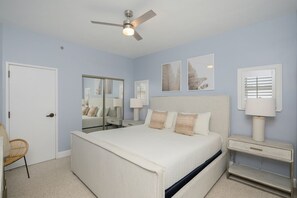 A bedroom with a bed, a ceiling fan, a nightstand, a chair, and artwork on the walls. - Tops'l 1111 2 Bedroom Condo by RedAwning (Miramar Beach)