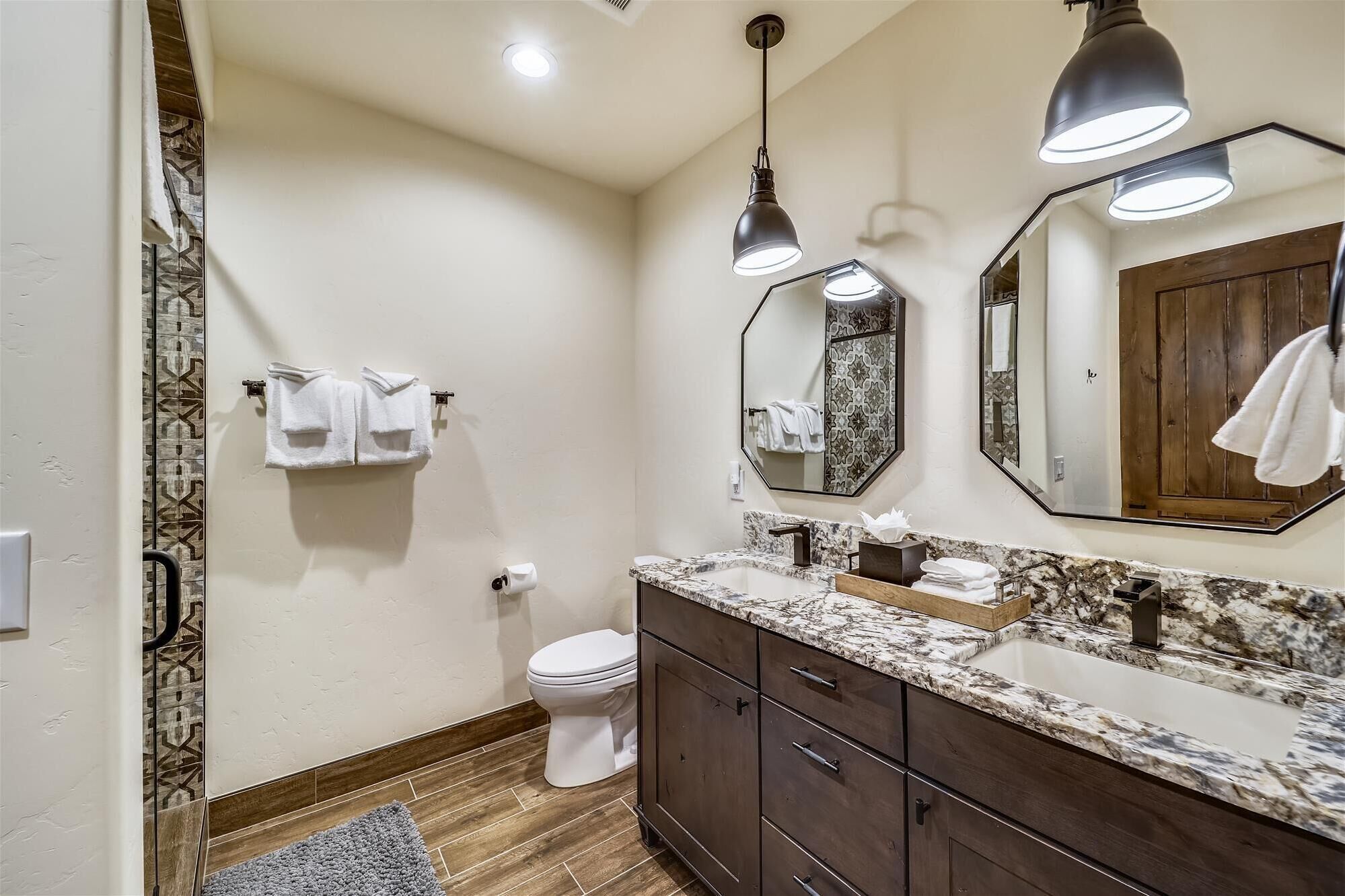 Une salle de bain moderne avec un lavabo en marbre, des meubles en bois foncé, des toilettes et deux lampes suspendues.