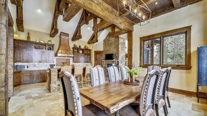 A rustic dining area with a wooden table and upholstered chairs, a stone fireplace, and a stone wall. - The Great Escape: Breckenridge Home with Hot Tub and Mountain Views (Breckenridge)