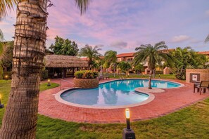A swimming pool surrounded by a brick patio, palm trees, and a thatched-roof structure. - Sweet 2 bedroom walking distance to Eagle Beach (Eagle Beach)