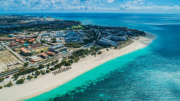 Vue aérienne d’une station balnéaire avec des propriétés situées en bord de mer, une plage de sable et un océan bleu et limpide.