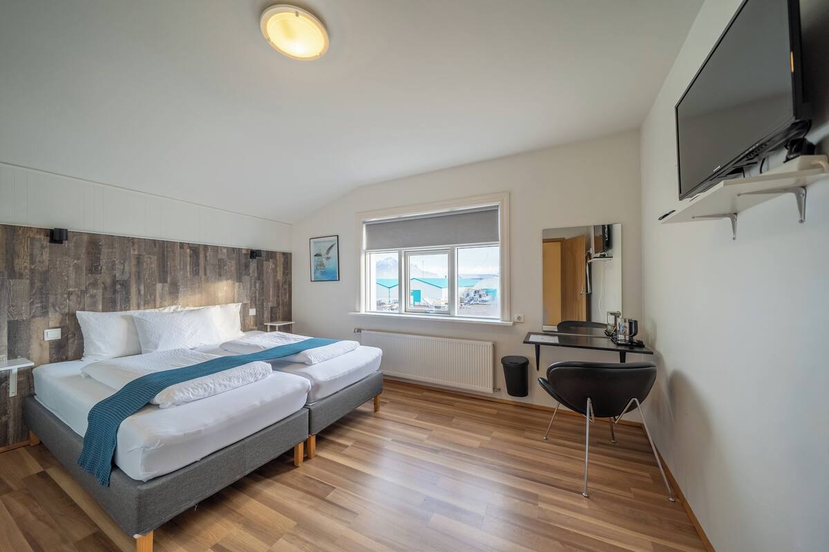 A modern bedroom with a bed, bedside table, TV, and a window with a view.