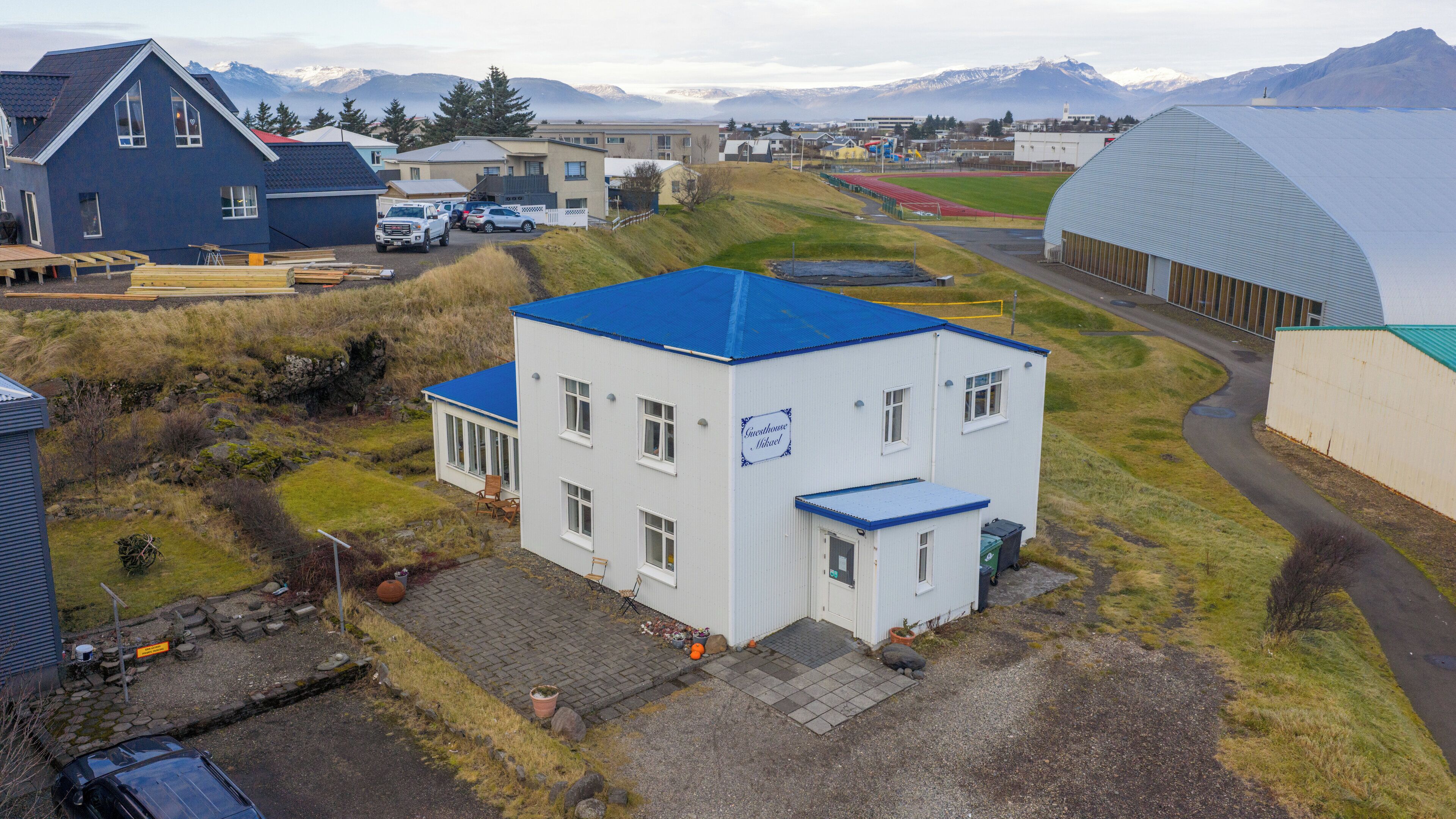 A white building with a blue roof, a sign reading "Sundasundhuset," and a paved driveway leading to a wooden deck.