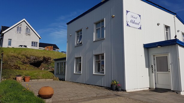 A hotel named "Hotel Mikael" with a corrugated metal exterior, a flat roof, and a paved entrance area with potted plants. - Guesthouse Mikael (Höfn)