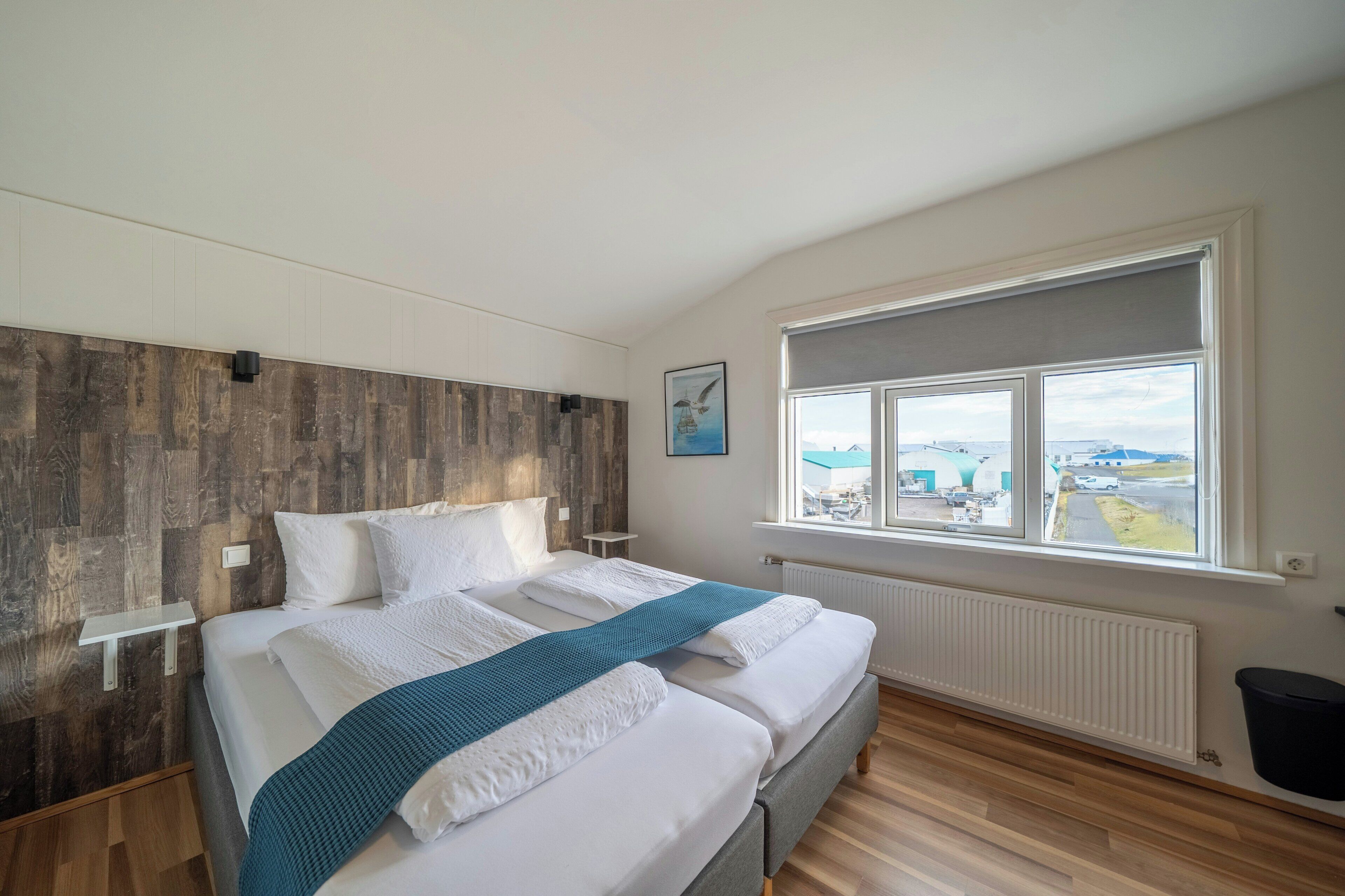 Un dormitorio con una cama, vistas de la ciudad a través de una ventana y un panel de pared de madera.