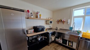 A modern kitchen with stainless steel appliances, a microwave, and a sink. There are shelves with various kitchen items and a window providing natural light. - Guesthouse Mikael (Höfn)