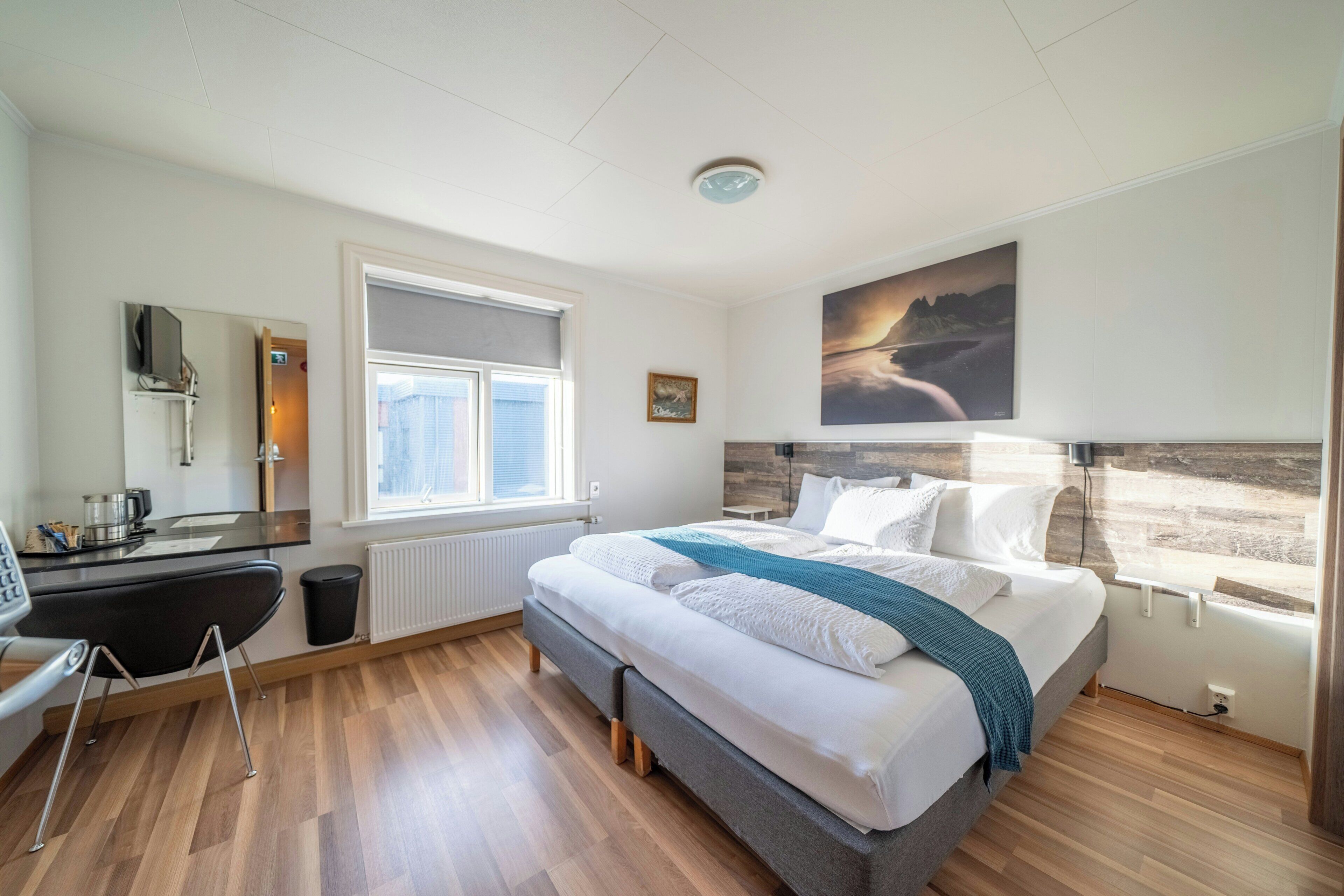 Habitación de hotel con cama, escritorio, silla, ventana y un cuadro en la pared.
