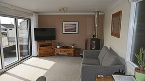 Ein Wohnzimmer mit einer Couch, einem Fernseher, einem Couchtisch aus Holz und einer Glastür, die auf einen Balkon führt.