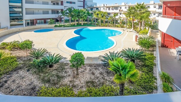 Un hôtel moderne doté d’une piscine centrale, entourée de palmiers et d’un espace paysager aménagé.