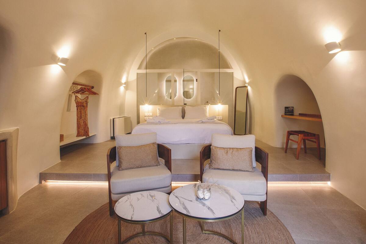 Ein Schlafzimmer mit einem großen Bett, zwei Sesseln, einem kleinen Tisch und einem Spiegel.