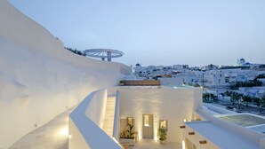 Un edificio moderno con facciata bianca, una terrazza sul tetto con una pergola e vista su una cittadina sullo sfondo.