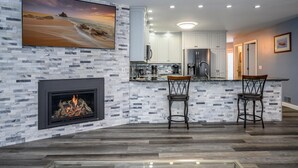 A modern kitchen with a stone backsplash, a fireplace, and a bar area with two stools. - Hiking, Hot Tub, Lake Front, Dock, Swimming (Canandaigua)