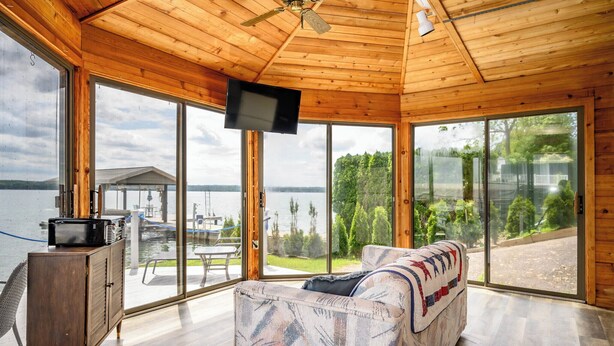 A wooden cabin with a large sliding glass door leading to a deck, a sofa, and a television mounted on the ceiling. - Hiking, Hot Tub, Lake Front, Dock, Swimming (Canandaigua)