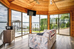 Une cabane en bois dotée d’une grande porte-fenêtre coulissante donnant sur une terrasse, d’un canapé et d’un téléviseur fixé au plafond.