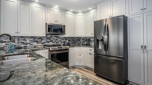A modern kitchen with white cabinets, a stainless steel refrigerator, a microwave, and a stove.