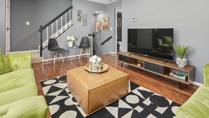 Una sala de estar moderna con una escalera, un televisor de pantalla plana y sillas tapizadas en verde.