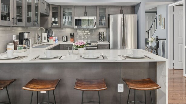 Una cocina moderna con armarios grises, electrodomésticos de acero inoxidable, una isla central con taburetes y una zona para desayunar.