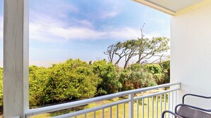 A balcony with a white railing overlooking a garden and a view of the sea. - Villa 389 2 bedroom, 1.5 bathroom (Jekyll Island)