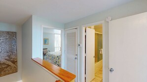 A hallway with a wooden bench, a white door, and a view into a bedroom with a bed and a map on the wall. - Villa 389 2 bedroom, 1.5 bathroom (Jekyll Island)