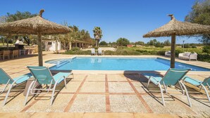 A pool area with lounge chairs and thatched umbrellas, surrounded by greenery and a clear sky. - Can Soler by Rentallorca (Porreres)