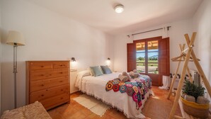 A bedroom with a bed, wooden dresser, lamp, and a view of the outdoors. - Can Soler by Rentallorca (Porreres)