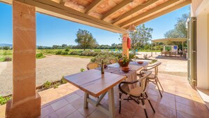 An outdoor patio with a table set for dining, a view of the countryside, and a covered area with outdoor furniture. - Can Soler by Rentallorca (Porreres)