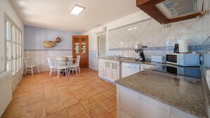 A kitchen with white cabinets, a granite countertop, a dining area with white chairs, and a tiled backsplash. - Can Soler by Rentallorca (Porreres)