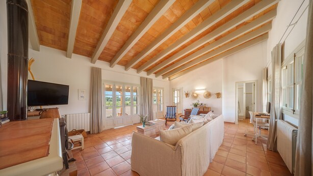 A spacious living area with a high wooden ceiling, a large sofa, a television, and a dining table. - Can Soler by Rentallorca (Porreres)