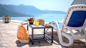 Eine Strandkulisse mit einer Liege, einem kleinen Tisch mit Getränken und Snacks sowie einer Handtasche am Boden.