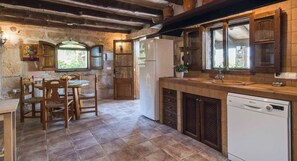 A rustic kitchen with wooden beams, a dining area with a round table and chairs, and a dishwasher. - Comteses Petit by Rentallorca (Alcúdia)