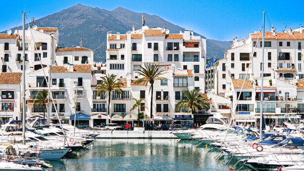 A marina with boats docked, surrounded by white buildings with orange roofs, and a mountain in the background. - Puerto Banus, 400 metres to the Beach (Marbella)