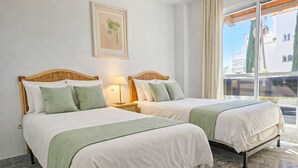 A hotel room with two beds, a nightstand with a lamp, a framed picture on the wall, and a view of the outside. - Puerto Banus, 400 metres to the Beach (Marbella)