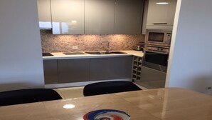 Eine kompakte Küche mit grauen Schränken, einer Granit Arbeitsplatte, einem Spülbecken und eingebauten Geräten, darunter eine Mikrowelle und ein Backofen.