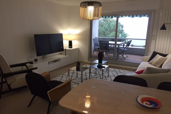 A modern living room with a flat-screen TV, a dining table, and a sofa.