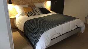 Ein ordentlich bezogenes Bett mit einem gemusterten Bettdeckenüberwurf, mehreren Kissen und einem Kopfteil an einer Wand.