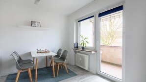 Een kamer met een witte tafel en twee stoelen, een radiator onder een raam, en een blauw vloerkleed.